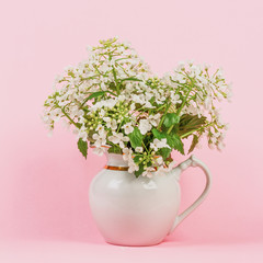 bouquet of white forest flowers in a white jug on a pink background close-up