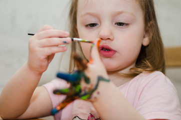 little girl carefully paints her hand with brush
