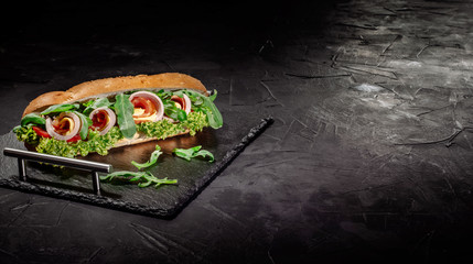 Huge fresh crispy baguette sandwich with meat, prosciutto, cheese, lettuce salad and vegetables on...