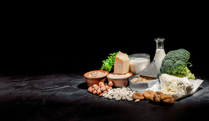 Foods rich in calcium such as sardines, bean, dried figs, almonds, hazelnuts, parsley leaves, broccoli, italian cabbage, cheese, milk, yoghurt on dark background