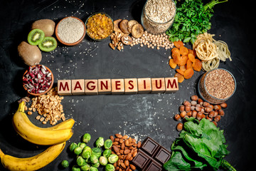 Assortment of high magnesium sources: bananas, nuts, oatmeal, buckwheat, peanuts, spinach chard, dark chocolate and sesame seeds on dark background