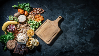 Assortment of high magnesium sources: bananas, nuts, oatmeal, buckwheat, peanuts, spinach chard, dark chocolate and sesame seeds on dark background