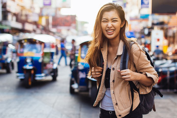 Young Asian female tourist woman with smile walking and backpacking on Khaosan road in Bangkok,...