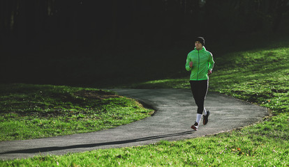 Fototapeta premium Horizontal outdoor shot of an athlete young man running on a trail. Athletic male jogging in the park in the morning in a sunny day. People, healthy lifestyle and sport concept