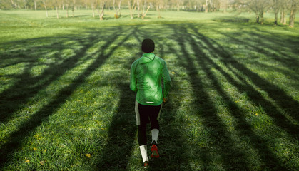Rear view of a young jogger man running on green grass in the forest. Athletic male jogging in the...