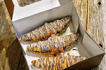 Croissants with chocolate and powdered sugar boxed and ready to go on rustic table top 
