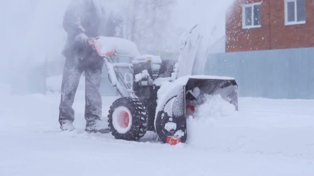 The man is removing snow with a snow blower in a blizzard. Slow motion.