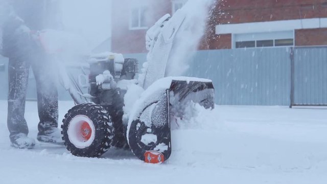 The man is removing snow with a snow blower in a blizzard. Slow motion.