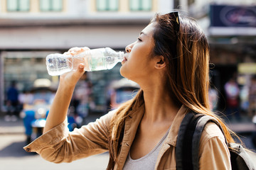 Young beautiful Asian female tourist woman drinking water from plastic bottle in city of Bangkok, Thailand