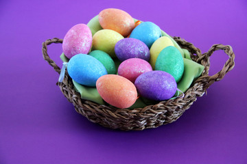 colorful shiny eggs in basket with purple background