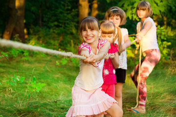 Group of happy children playing tug of war outside on grass. Kids pulling rope at park.