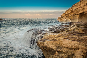 Fototapeta na wymiar Waves crash against rocks creating water cascade at St. Peter's Pool near Marsaxlokk, Malta