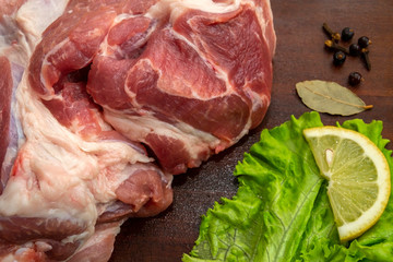 Fresh, raw pig meat prepared for cooking. Wooden chopping board with greens, lemon and spices. Cooking.