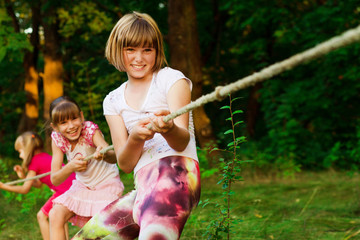 Group of happy children playing tug of war outside on grass. Kids pulling rope at park.