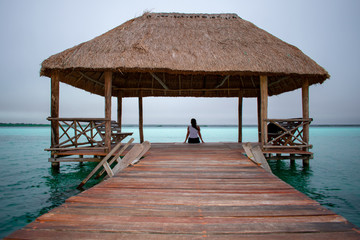 Back view of Young woman sits on wooden bridge on Bacalar Lake, Clear turquoise water in Mexico. 