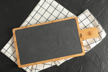 Cutting board with kitchen towel on black background, top view