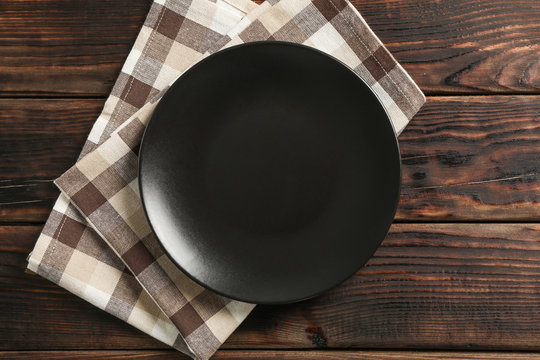 Kitchen towel with plate on wooden background, top view