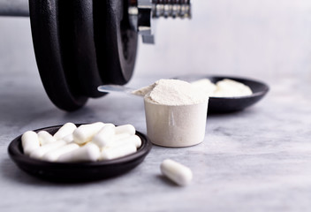 Scoop of Whey Protein, Creatine, Taurine capsules and a dumbbell. Bodybuilding food supplements on stone / wooden background. Close up. Copy space.