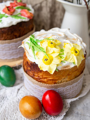 Easter cake kulich. Traditional Easter sweet bread decorated meringue, yellow daffodils on wooden gray background with lace fabric and colored egg. Copy space, selective focus.season's greetings card.