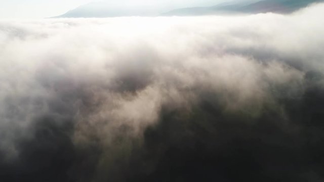 Aerial view of clouds and landscape under them. Shot. Top view of the clouds under the sky. Under the clouds shot from a bird's flight, the sun shines on the clouds