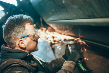 man in goggles for cutting metal, stpli with an electric rotating angle grinder and works by...