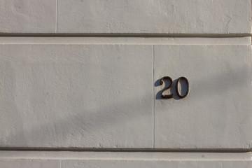 House number 20 on a white wall with shadow outside