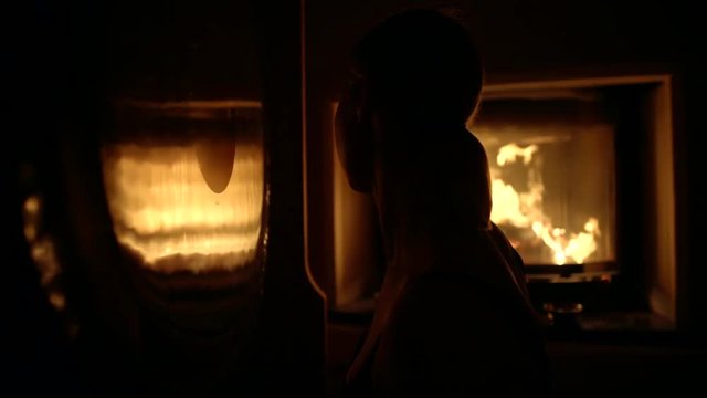 young chinese woman is hitting the large bronze gong in dark room with burning fireplace