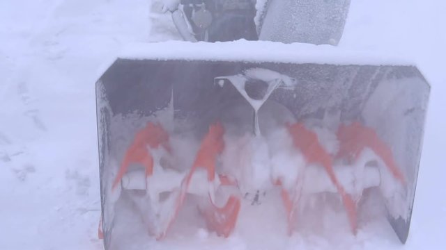 The spinning blades of the snowblower are milling much snow.