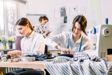 Portrait of young fashion dressmakers women at work. Dressmaker, tailor, fashion and showroom concept - Portrait of talented female dressmakers working with textile for sewing clothes