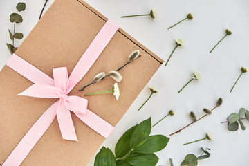 Spring composition with a gift box with a pink bow and green sprigs and flowers lying on a white background. Background, copy space for text, top view, close-up