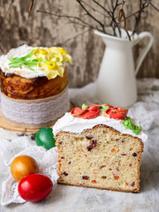 Easter cake kulich. Traditional sweet bread decorated meringue, yellow daffodils on gray background with lace fabric and colored eggs. Copy space, selective focus.Slice of cake.season's greetings card