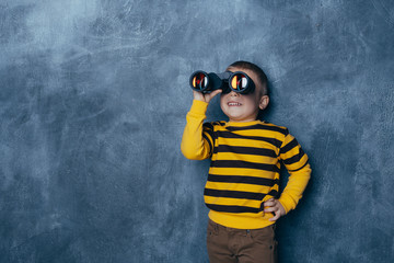 Little boy looking through binoculars on a dark blue background with a happy face standing