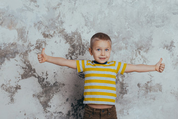 Naklejka premium Young boy child in a yellow striped T-shirt celebrating a happy smiling laugh with a hand spread over