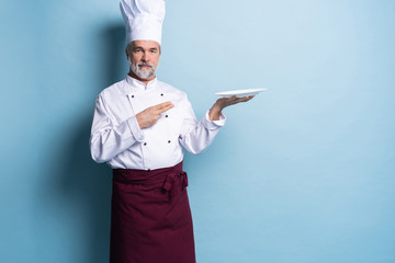 Portrait of a professional chef holding an empty plate isolated on light blue.