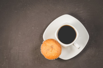coffee break. White cup of the hot black coffee and cupcake on a dark background copy space, top view. Breakfast concept