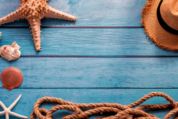 From above summer hat near rope and sea stars with seashells on blue wooden background