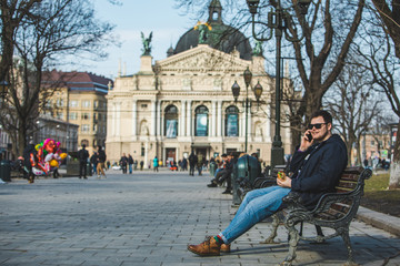 Obraz premium man eating burger surfing internet on phone sitting on bench