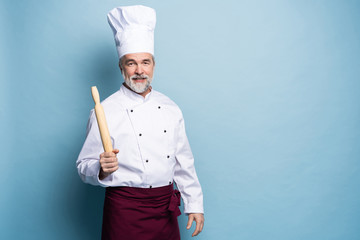 Mature professional chef with rolling pin on blue background.