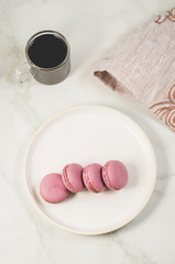 sweet macaroons or macaron on a white bowl and coffee in a glass on a white background, top view. French dessert