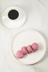 sweet macaroons or macaron in a white bowl and coffee cup on a white background, top view. French dessert