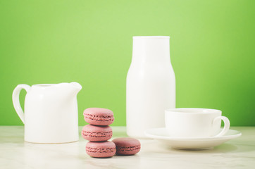 sweet macaroons or macaron, coffee cup, white creamer and bottle on a green background.  French dessert