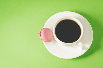sweet macaroons or macaron and coffee white cup on a green background, top view and copy space. French dessert