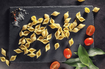 Pasta shells on black stone. Tomatoes and bay leaves with allspice and sea salt.