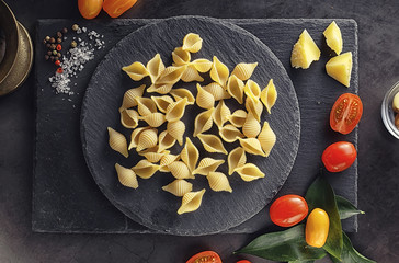 Pasta shells on black stone. Tomatoes and bay leaves with allspice and sea salt.