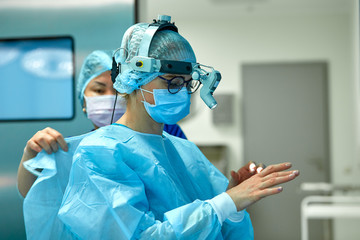 Surgeons wear sterile clothing before surgery. A team of surgeons preparing for surgery, set up additional light on the head.