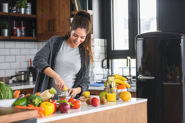 Beautiful smiling young pregnant woman preparing healthy food with lots of fruit and vegetables at home kitchen