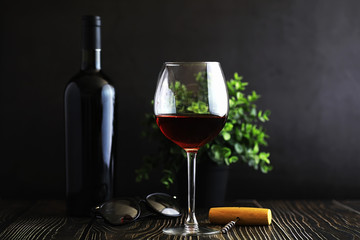 A glass of red dry wine on the table. Dark bottle and glass of wine.