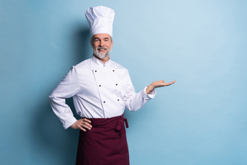 Portrait of a happy chef cook showing copyspace on the palms isolated on light blue background.