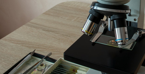 Microscope on the desk of the biologist with the micro-specimens, a scalpel and tweezers.