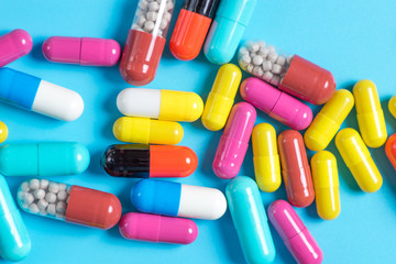 Green, yellow, red and pink pills or capsules on a blue background